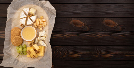Cheese plate with honey, grapes and nuts on wooden background, top view