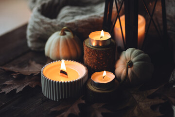 Cozy autumn composition with aromatic candle, pumpkins, wool sweater, leaves, cinnamon. Aromatherapy on a grey fall morning, home atmosphere of cosiness and relax. Wooden background close up.