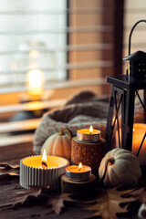 Cozy autumn composition with aromatic candle, pumpkins, wool sweater, leaves, cinnamon. Aromatherapy on a grey fall morning, home atmosphere of cosiness and relax. Wooden background close up.