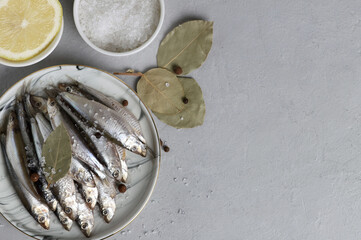 Freshly salted fish with pepper, bay leaf and lemon on a light plate on a gray background. Top view. Traditional Spanish cuisine: sardines. Copy space.