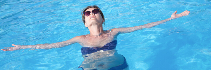 Young woman in sunglasses swimming and relaxing in pool top view
