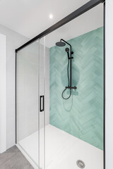 Modern bathroom with aquamarine and white tiles, rain head, hand held shower and glass door.