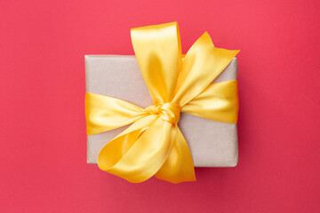 Beautiful gift box with a yellow bow and brown craft paper. Top view. Flat lay. Red background.