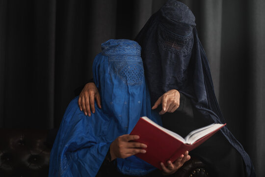 Afghan Muslim women with burka traditional costume, reading holy  Quran against the dark background