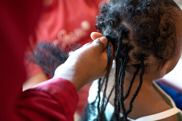 African hair stylist braided hair of African pigtails for little baby girl, selective focus