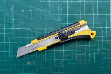 Old used green cutting mat and construction knife. Top view.