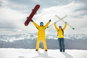 Couple of skier and snowboarder are standing at mountain top, holding ski and snowboard in hands...