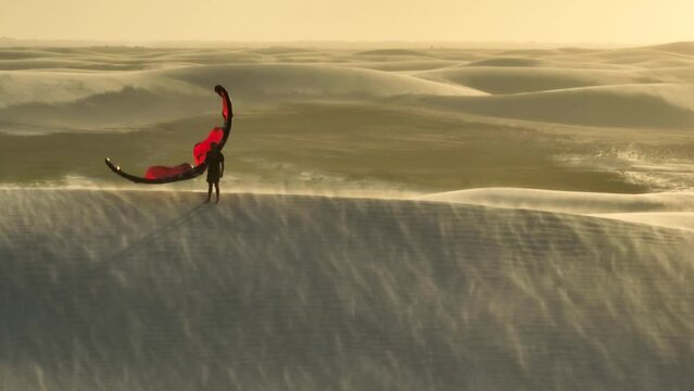 Tracking 360 Degree Aerial Drone Shot of Man Holding Red Kitesurfing Kite During Sunset on a Wind Swept Dune 