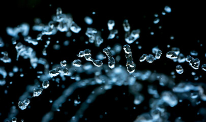 Drops of water splash blue water on a black background, concept of freshness drink, watering the rain source of pure water fountain copy space