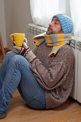 Man with hat, sweater and hand gloves indoors on a chilly winter day, energy and gas crisis, cold...