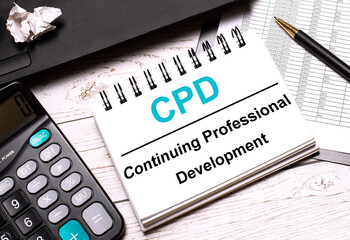 On a light-colored office table is a computer, a black calculator, a pen, and a notebook with the text CPD Continuing Professional Development