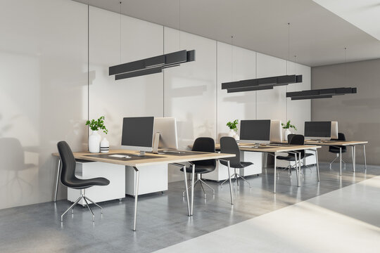 Perspective view on sunlit coworking office work places with modern computers on wooden tables, black lamps and chairs and grey concrete floor. 3D rendering