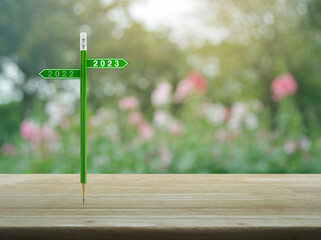 2023 and 2022 direction sign plate with green pencil on wooden table over blur pink flower and tree in garden, Business happy new year 2023 planning cover concept