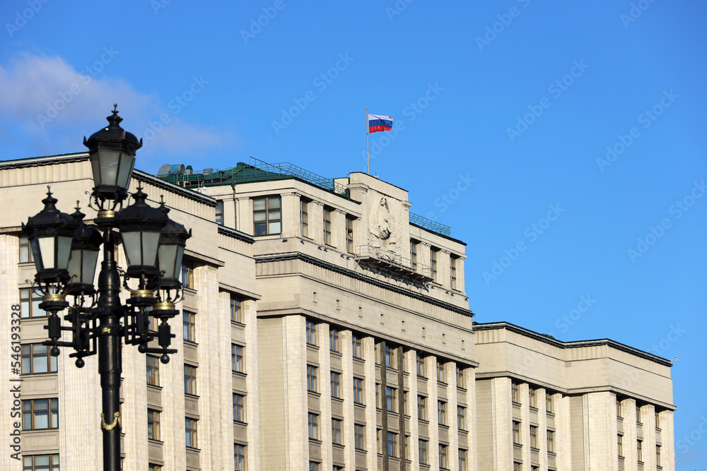 Wall mural Parliament building in Moscow with Russian flag on background of blue sky. Facade of State Duma of Russia with soviet coat of arms, russian authority