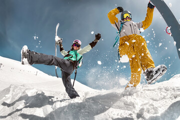 Happy couple of snowboarders are having fun and jumps with snowboards in hands. Winter holidays at...
