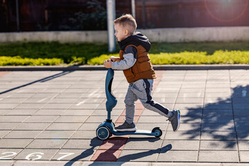 Fast little boy is riding scooter on a street.
