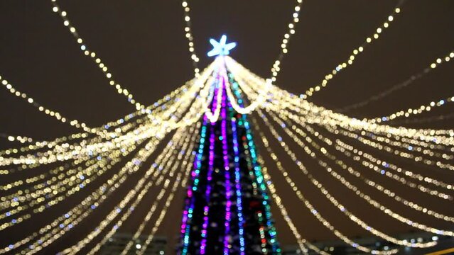Blurred Christmas tree with multi-colored and golden bokeh lights of garland at night