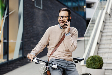 An eco urban businessman is leaning on his bicycle on the street and talking on the phone.