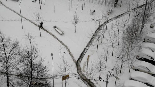 A man walks along a road cleared of snow in yard of city (top view)