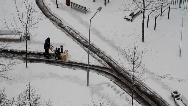 Worker removes snow with a snow blower in yard of city (top view)