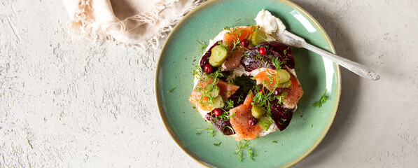 plate with bagel with cream cheese, beets, gherkins and salmon on a light table