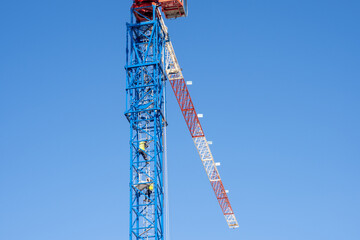 Workers climb the tower crane. The crane operator climbs the metal ladder to the workplace. Builders mount a crane at a construction site.