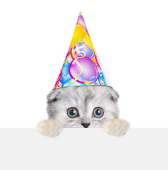 Cute kitten wearing party cap looks above empty white banner. isolated on white background