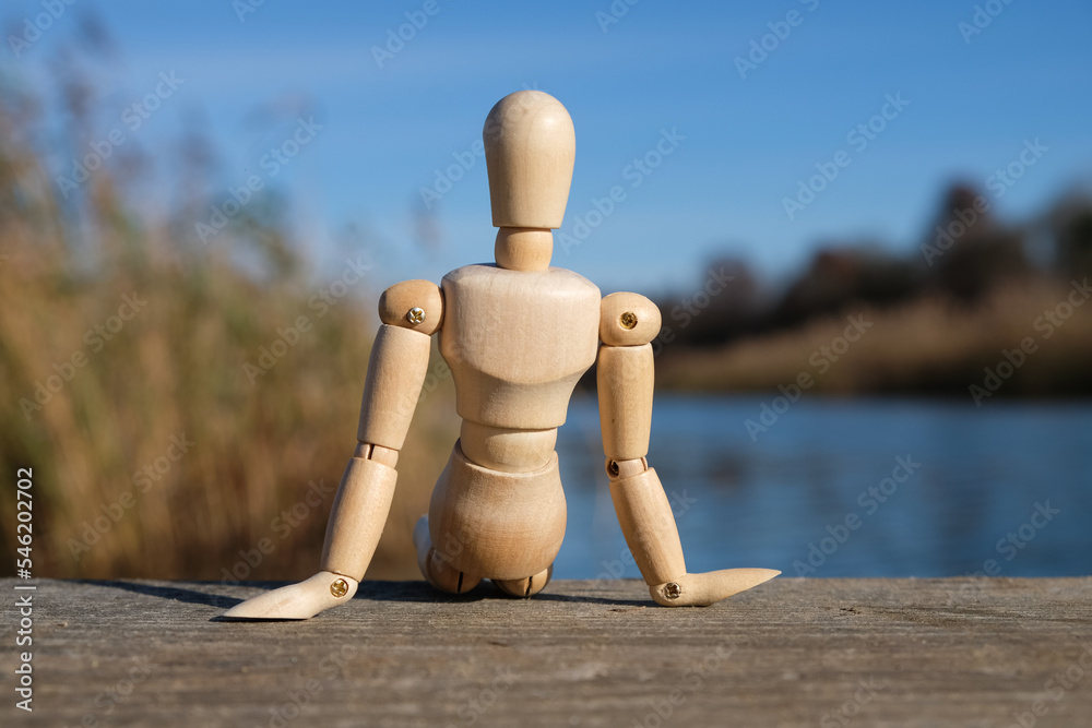 Wall mural A wooden doll sits on a river bridge. Back view.