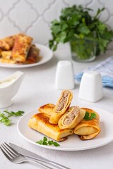 Thin pancakes stuffed with boiled minced meat with fried onions on a white plate on a light concrete background. Pancake recipes.