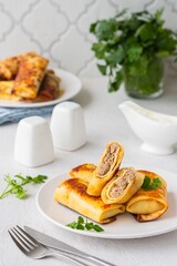 Thin pancakes stuffed with boiled minced meat with fried onions on a white plate on a light concrete background. Pancake recipes.