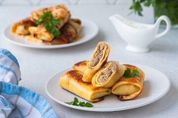 Thin pancakes stuffed with boiled minced meat with fried onions on a white plate on a light concrete background. Pancake recipes.
