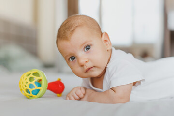 close-up of a baby girl 2 months old, lies on her stomach with a rattle, looks at the camera, the concept of newborn, infancy