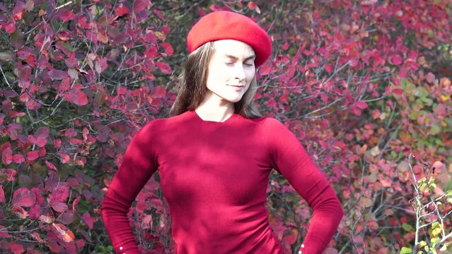Young beautiful sensual woman in a red sweater and beret posing in the autumn forest, against a background of red foliage. Fashionable video portrait