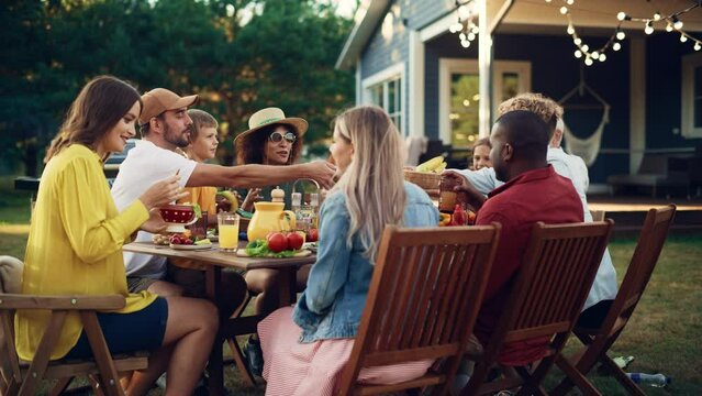 Group of Multiethnic Diverse People Having Fun, Communicating with Each Other and Eating Vegetarian Meals at an Outdoors Dinner. Relatives and Friends Gathered Outside Their Home on Warm Summer Day.