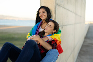 Happy lesbian young couple embraces and holds a rainbow flag. LGBT community.