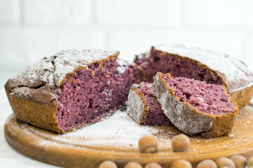 Homemade cake with raspberries and hazelnuts sprinkled with powdered sugar on a wooden background
