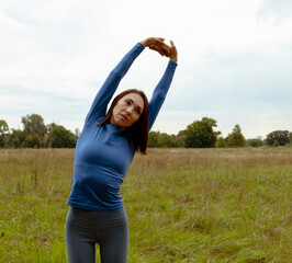 Athletic Asian woman in a sweater doing stretching in the field. Workout woman. Workout nature. Asian woman portrait