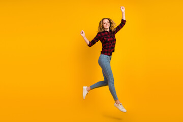 Fototapeta na wymiar Full length view of glad cheerful wavy-haired girl jumping having fun fist up isolated on bright vivid shine background