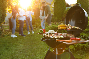 Group of friends having party outdoors. Focus on barbecue grill with food. Space for text