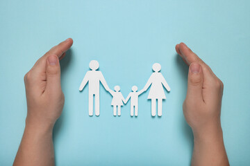 Fototapeta na wymiar Man protecting paper family figures on light blue background, top view. Insurance concept
