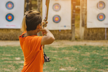 Back view of Asian boy wear face mask aims archery bow and arrow to colorful target in shooting...