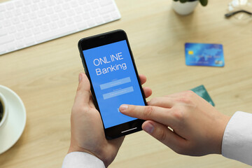 Man using online banking app on smartphone at wooden office table, closeup