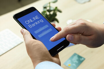 Man using online banking app on smartphone at wooden office table, closeup