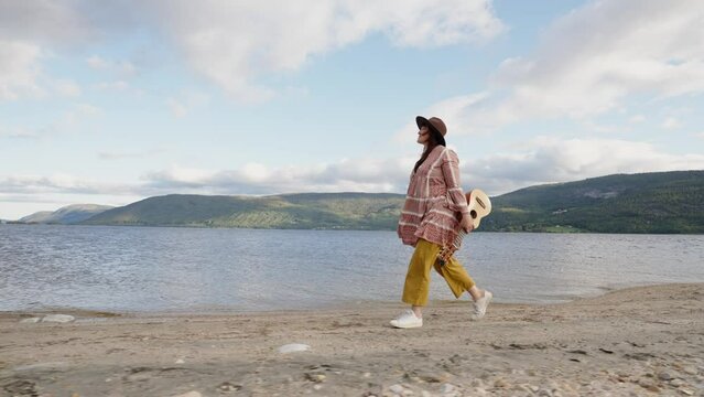 hipster woman is walking along beach. Enjoy cloudy day. Leisure in nature, enjoyment and relaxation.
