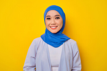 Close-up of smiling young Asian Muslim woman looking at camera isolated over yellow background