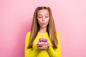 Photo of funky pretty school girl dressed yellow top blowing candle fire cake piece making wish isolated pink color background