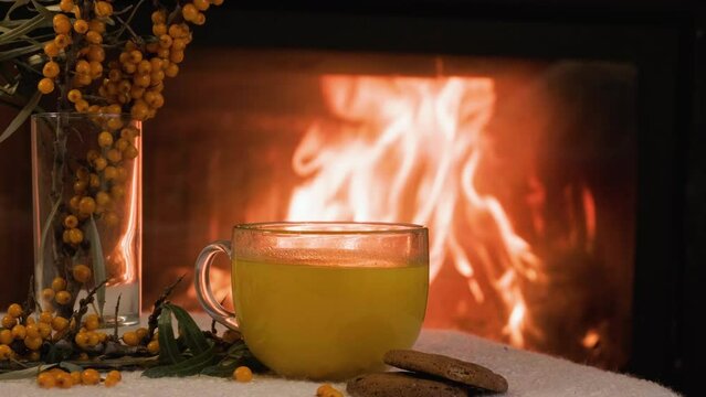 A cup of tea with sea buckthorn on the background of a fireplace