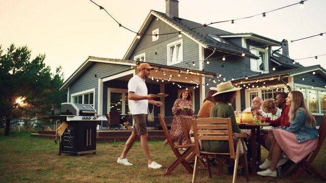 Big Family and Friends Celebrating Outside at Home. Diverse Group of Children, Adults and Old People Gathered at a Table, Having Fun Conversations. Preparing Barbecue and Eating Vegetables.