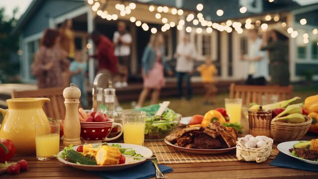 Outdoors Dinner Table with Gorgeous-Looking Barbecue Meat, Fresh Vegetables and Salads. Happy Joyful People Dancing to Music, Celebrating and Having Fun in the Background on Home Porch.