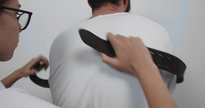 Young nurse in glasses and white coat with long dark hair undoing knots and unfastening straps on straitjacket, freeing bearded male patient. Treatment of schizophrenia in psychiatric clinic